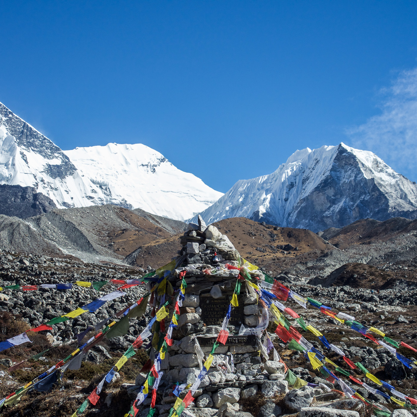 Steinmal mit bunten Gebetsfahnen vor schneebedeckten Himalaya-Gipfeln.